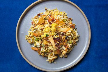 A plated portain of Biryani on a pale purple plate on a bright blue background