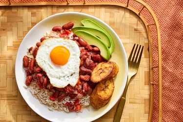 Overhead view of Colombian beans and rice on a plate and a wooden tray with a fried eggs