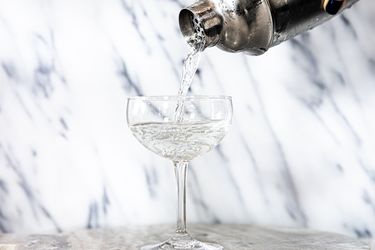 a cocktail being poured in a coupe glass from a cobbler shaker