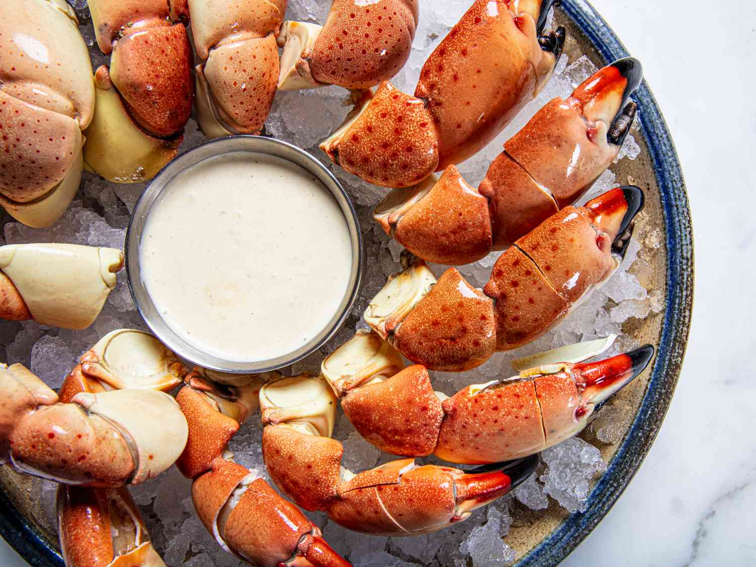 Mustard dip surrounded by cracked stone crab claws on ice in a bowl with a blue rim