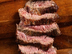 A piece of medium-rare steak sliced into thin pieces on a wooden cutting board.