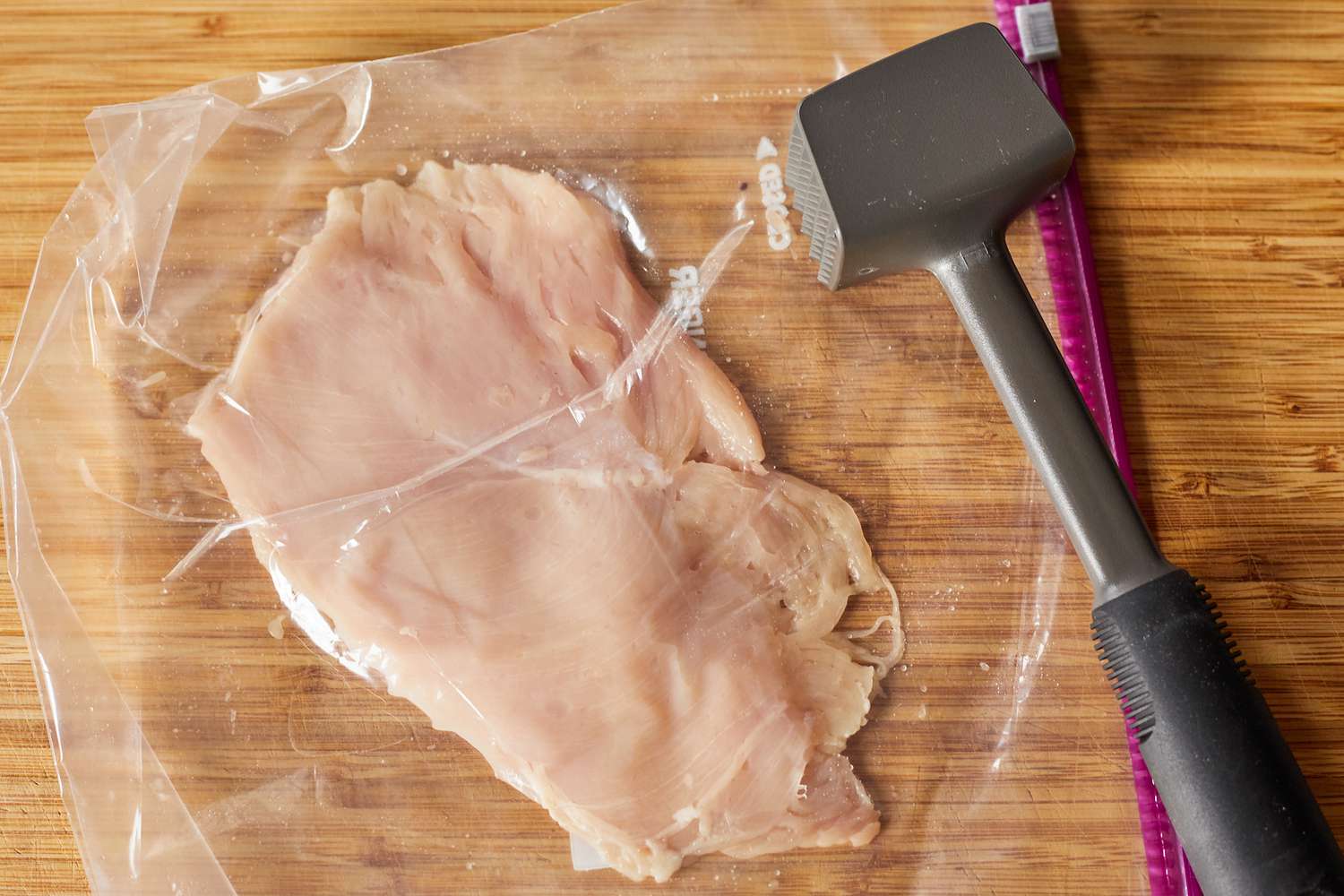 a meat pounder sitting beside a flattened chicken breast