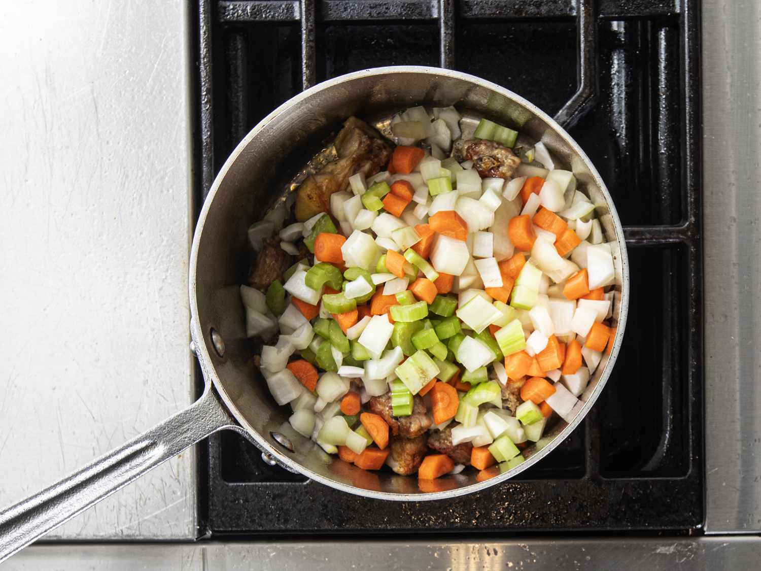 Vegetables and chicken back pieces sautÃ©ing in pan to make jus.