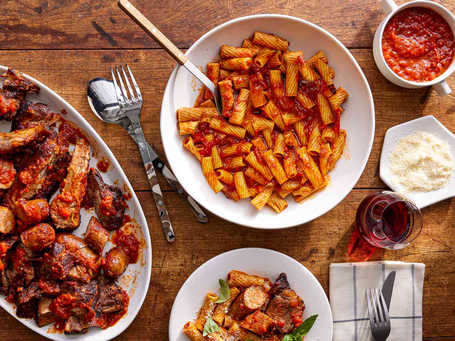 Overhead view of a tablescape of Ragu Napoletano with pasta, a single serving, the platter of meat, extra sauce and extra cheese