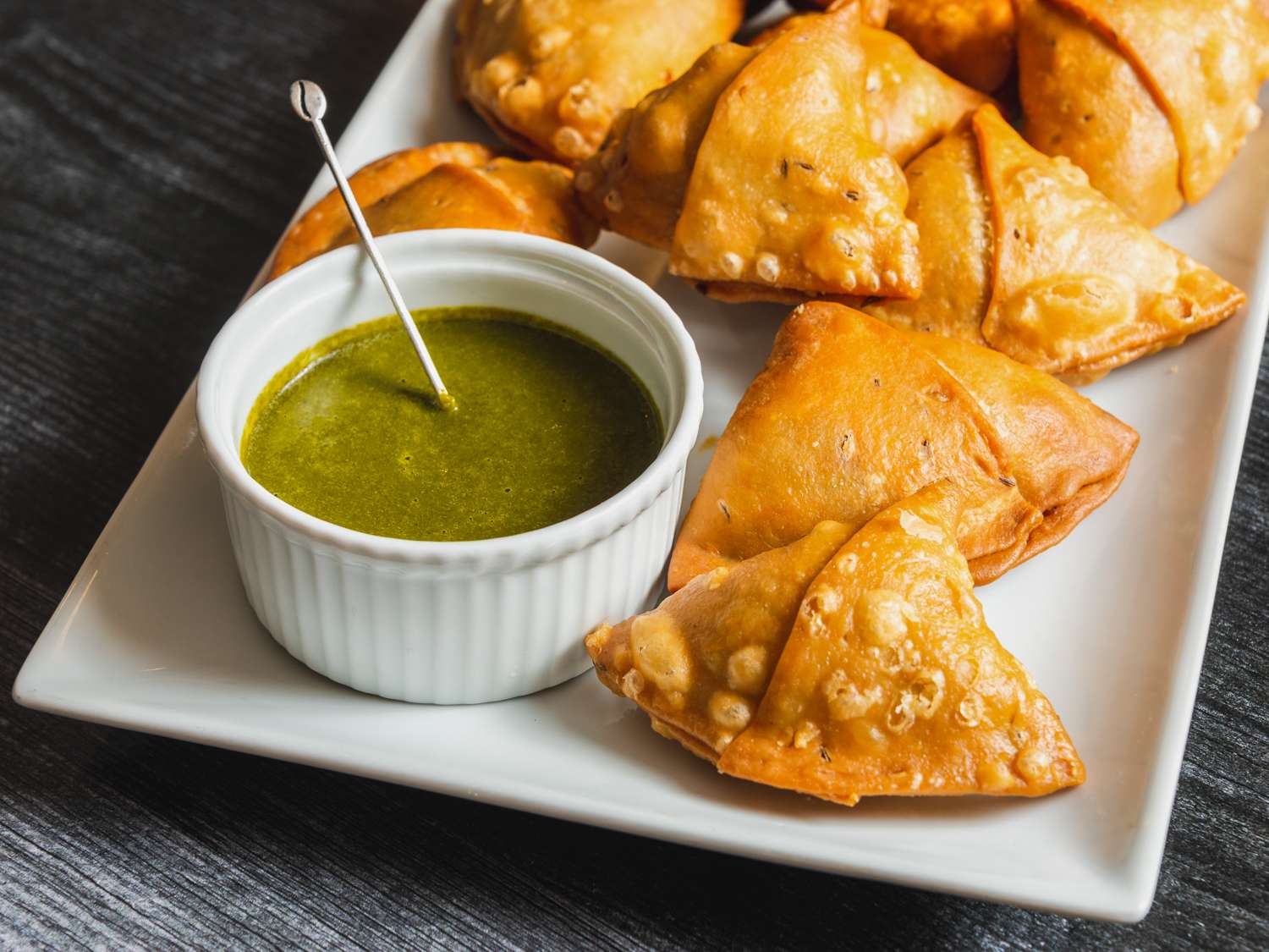 Samosas on a serving plate with a ramekin of herb chutney alongside