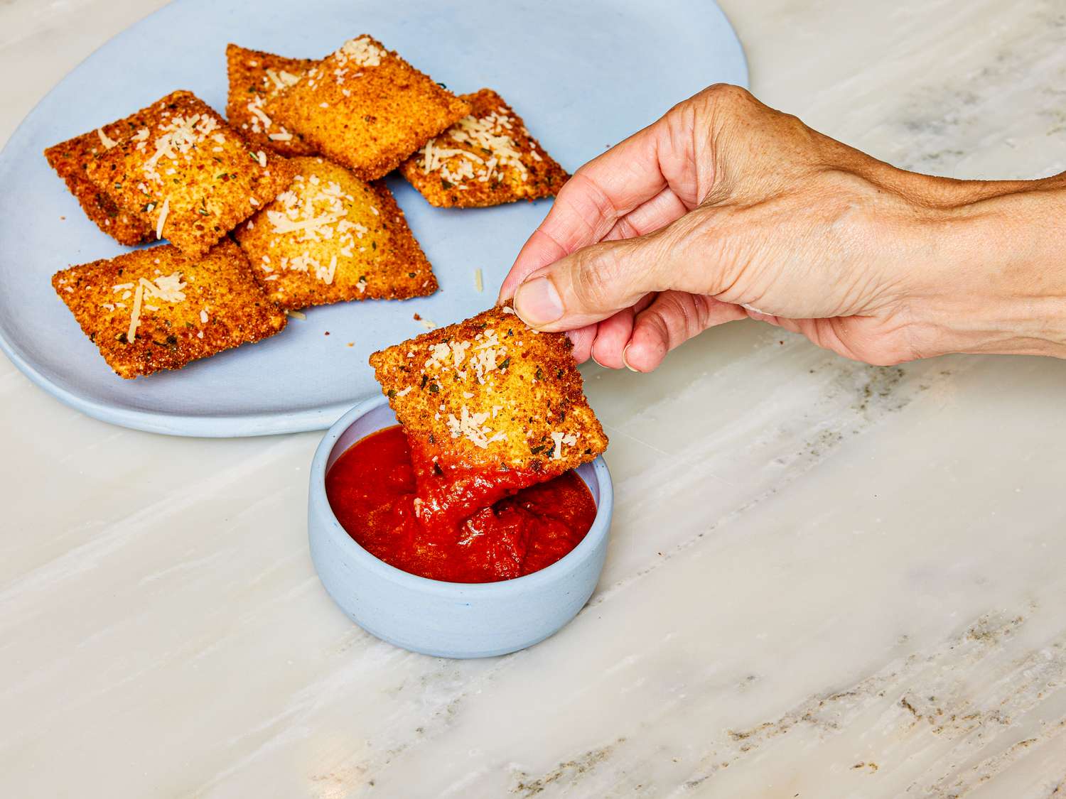 Side view of dipping toasted ravioli into marinara sauce