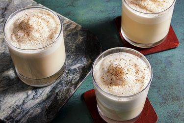 Three glasses of eggnog on a green surface with red coasters