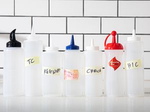 7 squeeze bottles lined up in front of white tiles.