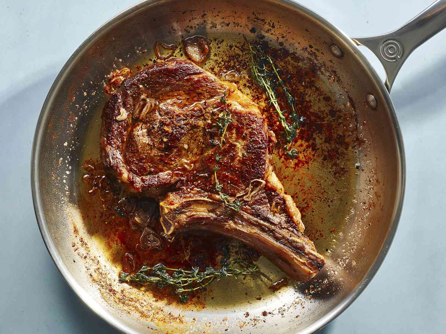 A seared bone-in rib eye with aromatics in a stainless steel skillet.