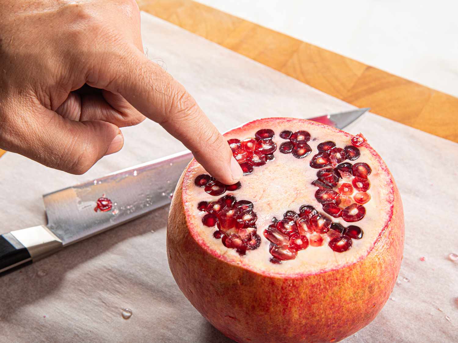 Side view of a hand pointing out the pith of a pomegranate