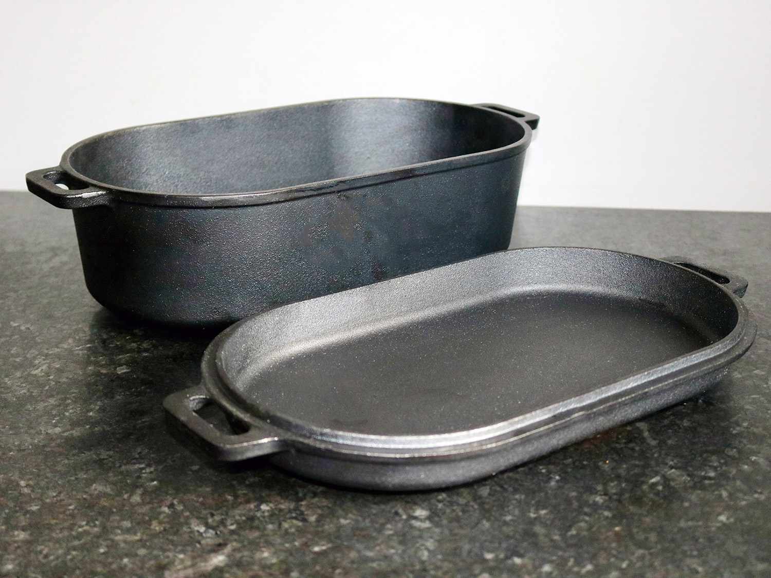 a cast iron roasting pan and lid sit on a counter side by side