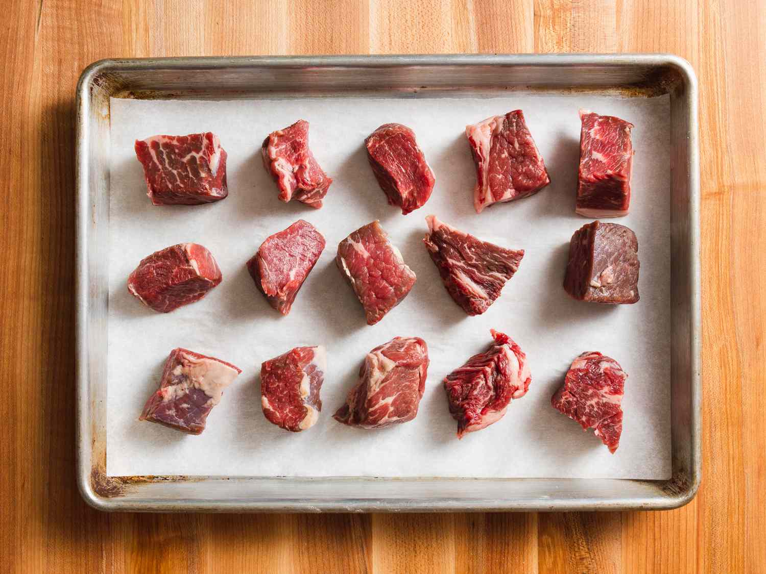 Chunks of meat on a parchment-lined baking sheet