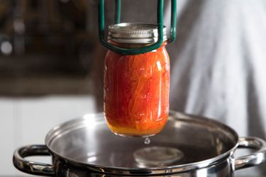 A jar of processed tomatoes being removed from a water bath with a pair of jar tongs.