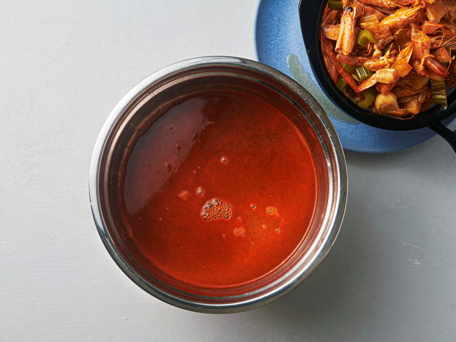 Strained stock with residual oil on top, with fine mesh strainer next to it