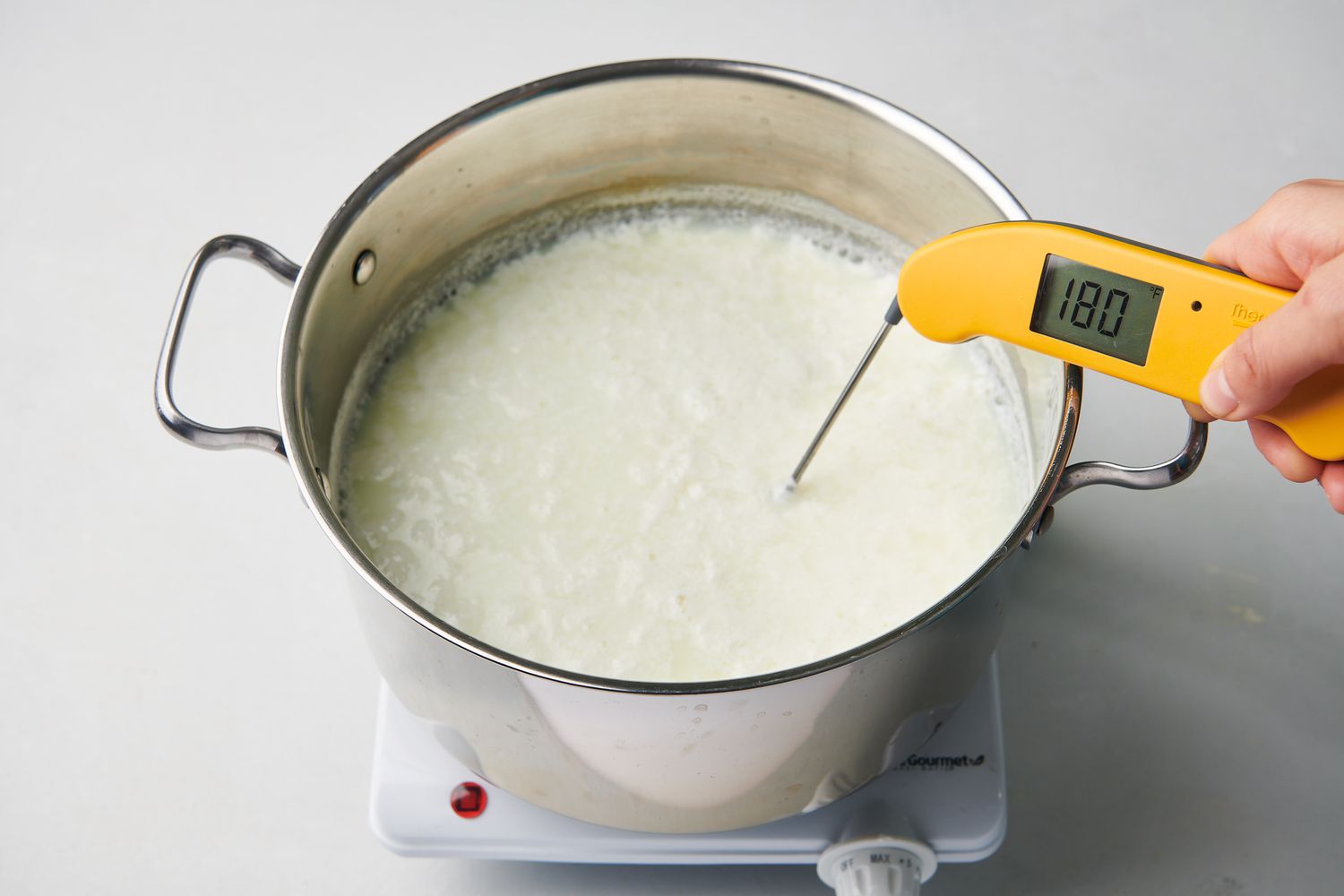 An instant-read thermometer inserted into curdled-milk mixture.