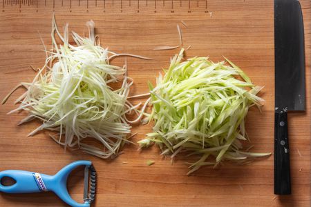 Knife-cut and peeler-shredded green papaya on a cutting board