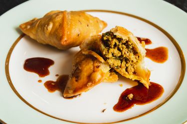 盘子里放着两个kheema samosa，其中一个打开了，露出了内部