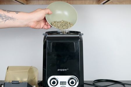 green coffee beans being loaded into the top of an air coffee roaster