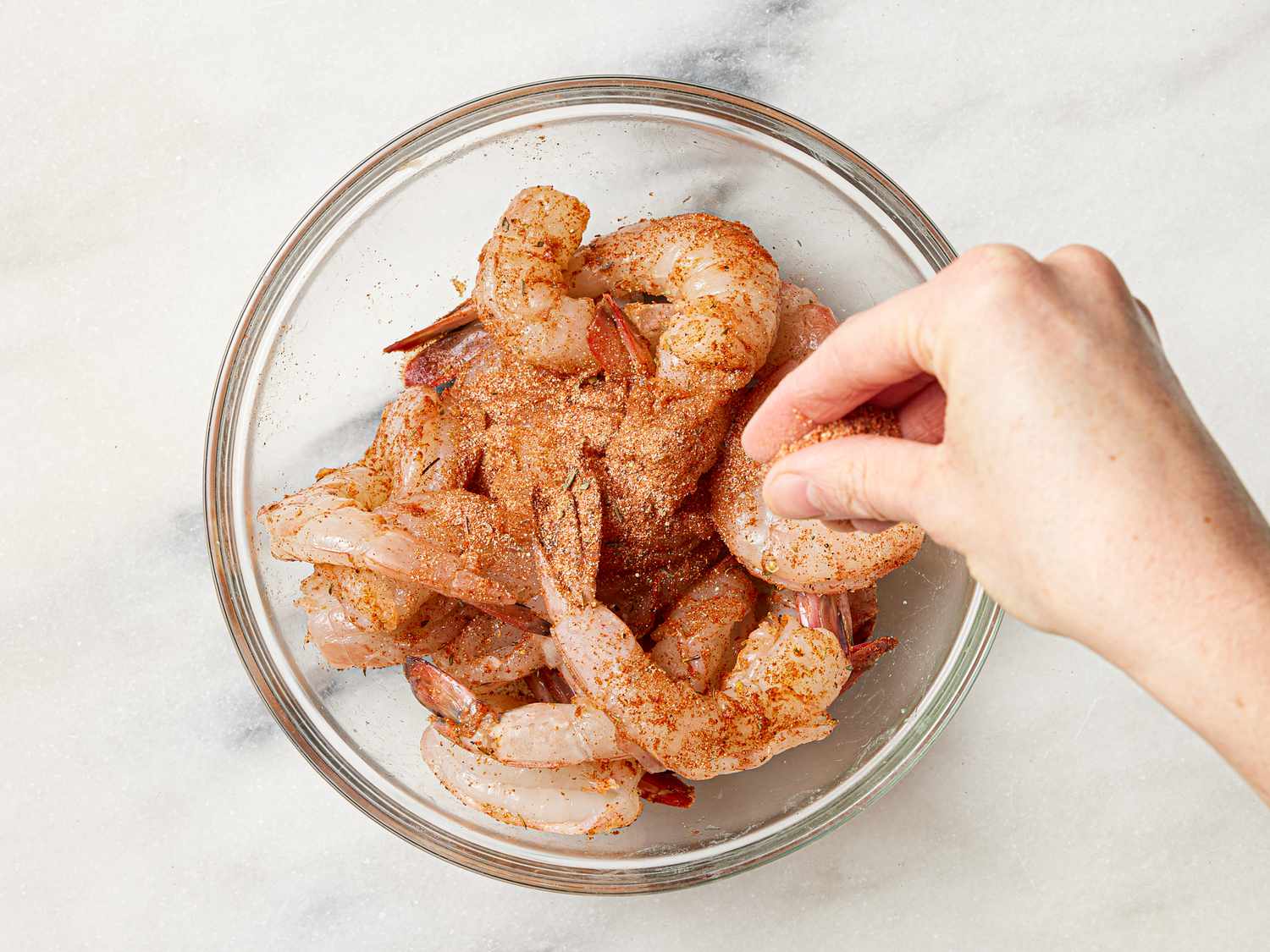 Shrimp in a glass bowl being tossed with Cajun seasoning.