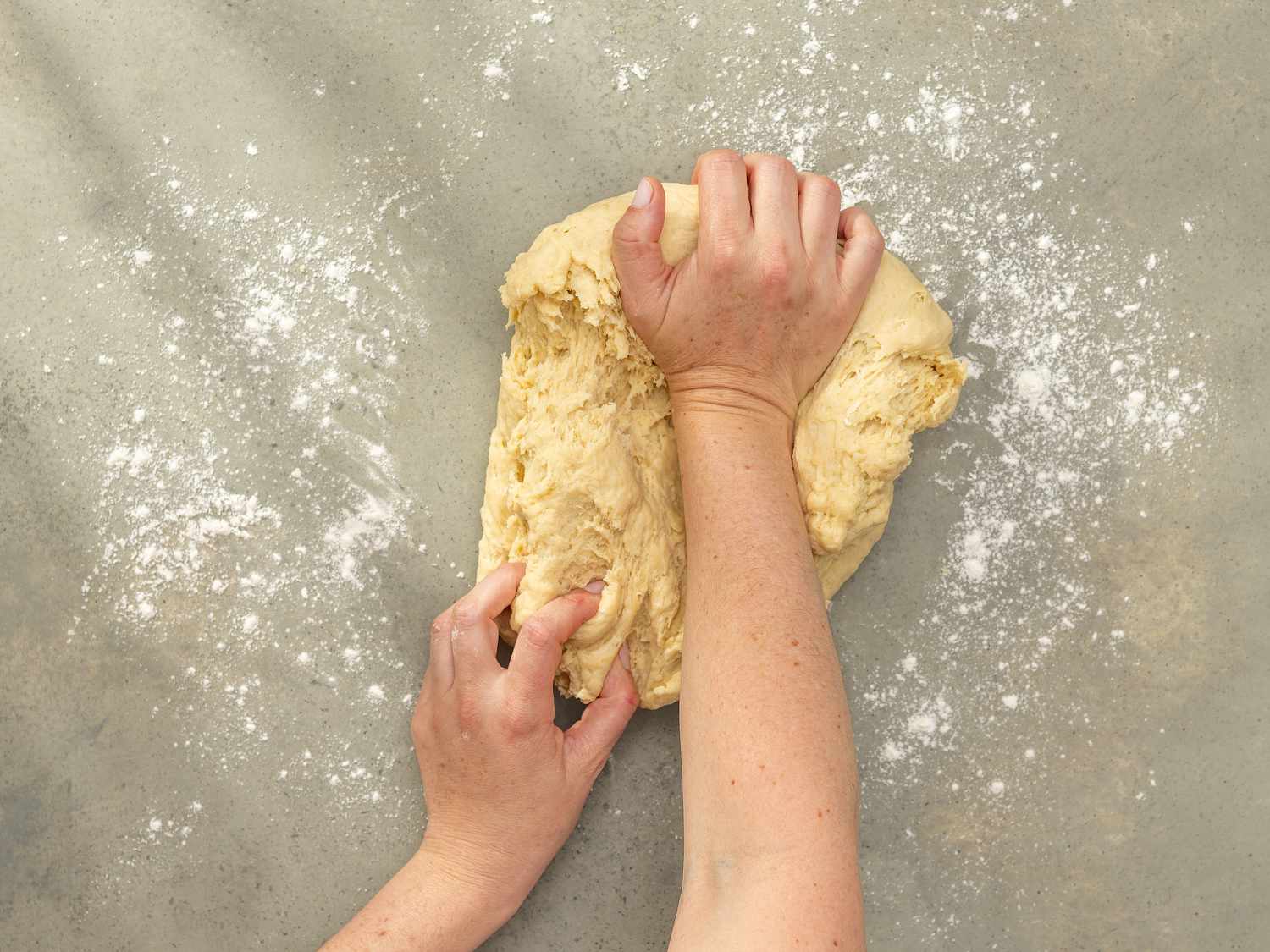 Overhead view of hands kneading dough on a floured surface