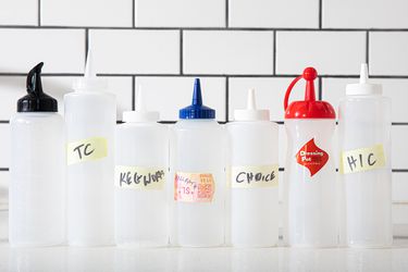 7 squeeze bottles lined up in front of white tiles.