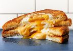 Two halves of a grilled cheese egg-in-the-hole sandwich stacked on top of each other, with cheese and egg overflowing from the middle.