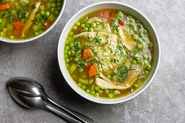 Chicken and rice soup fills two white bowls. Two spoons lay beside them.