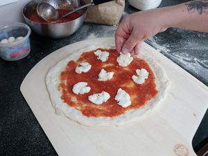 a hand topping mozerella on a pizza on top of a wooden pizza peel