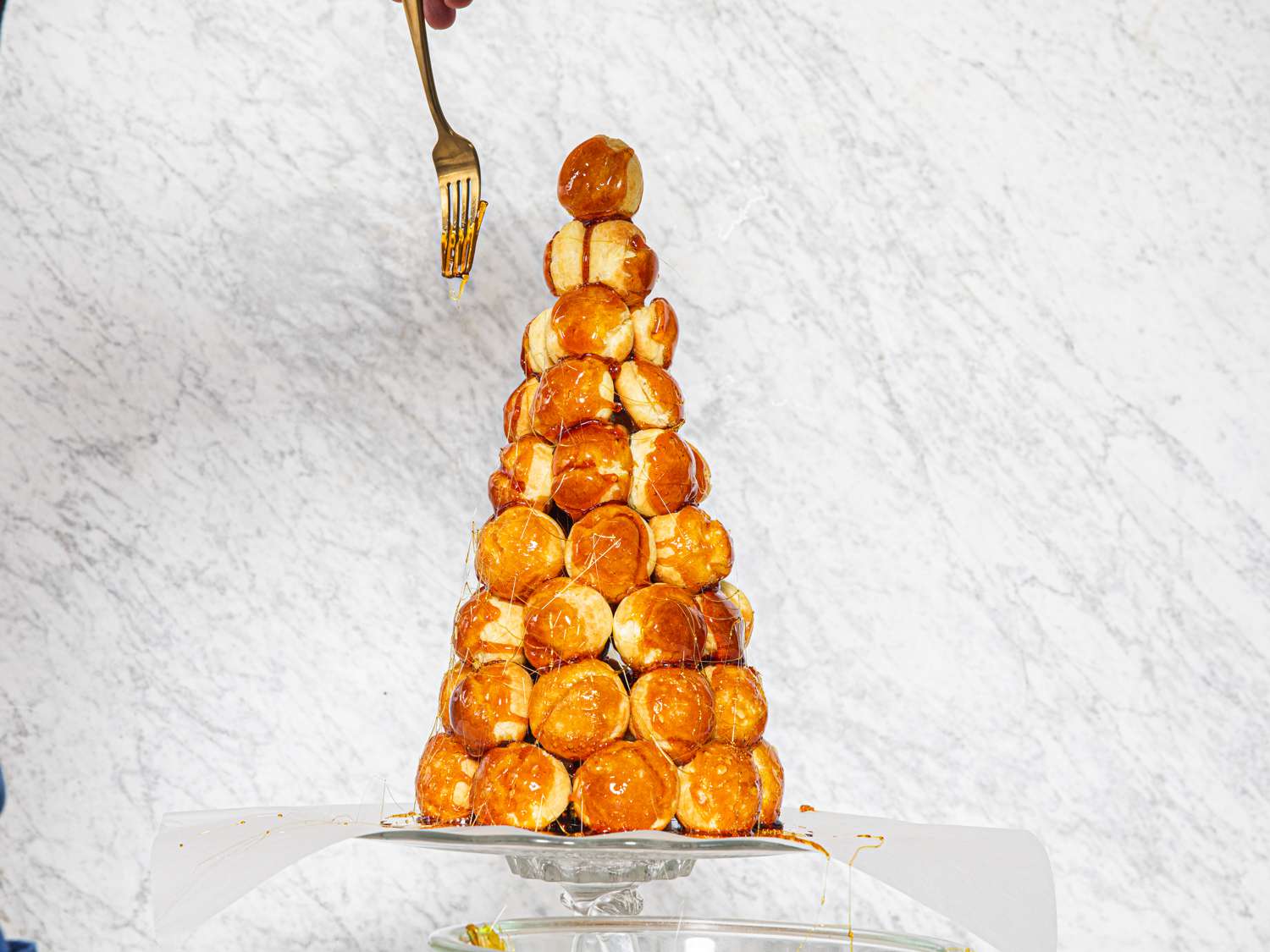 A fork drizzling carmel on croquembouche