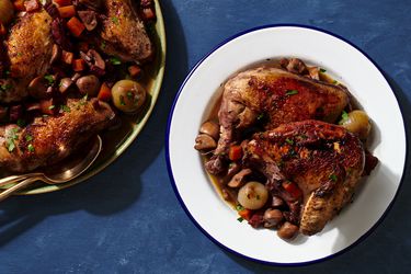 白色,blue-rimmed板夹持一个大of Coq au Vin. On the lefthand side of the image is a round platter holding more of the Coq au Vin.