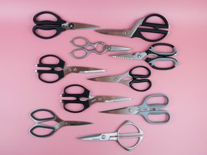 ten different kitchen shears lined up on a pink background