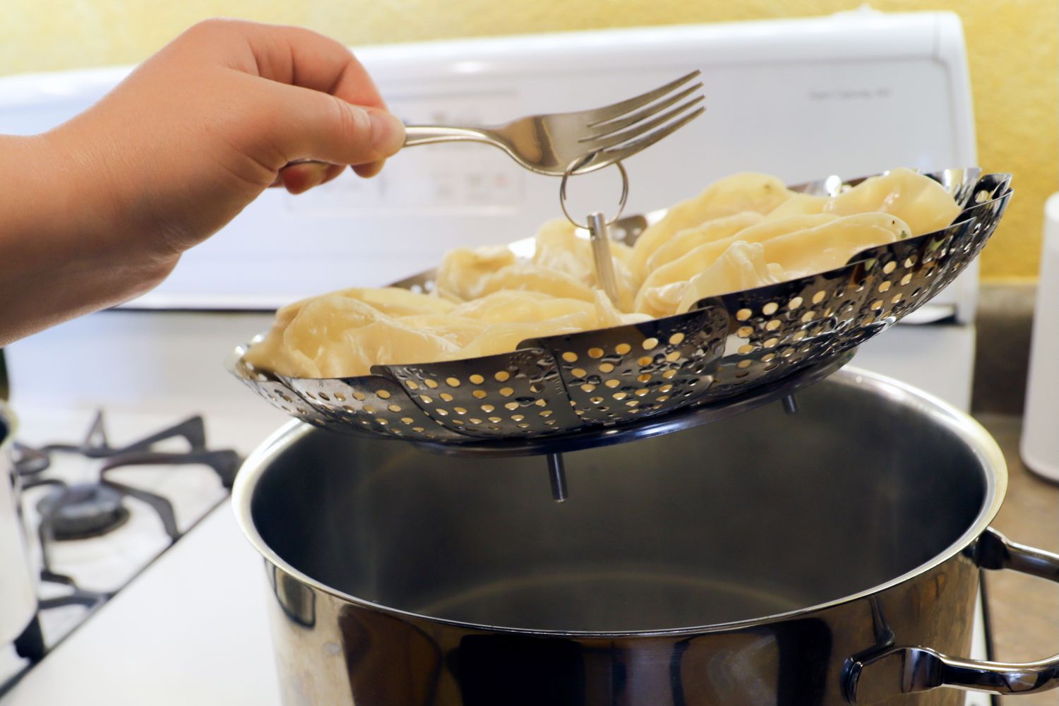 a fork lifting a steamer basket filled with dumplings out of a stockpot