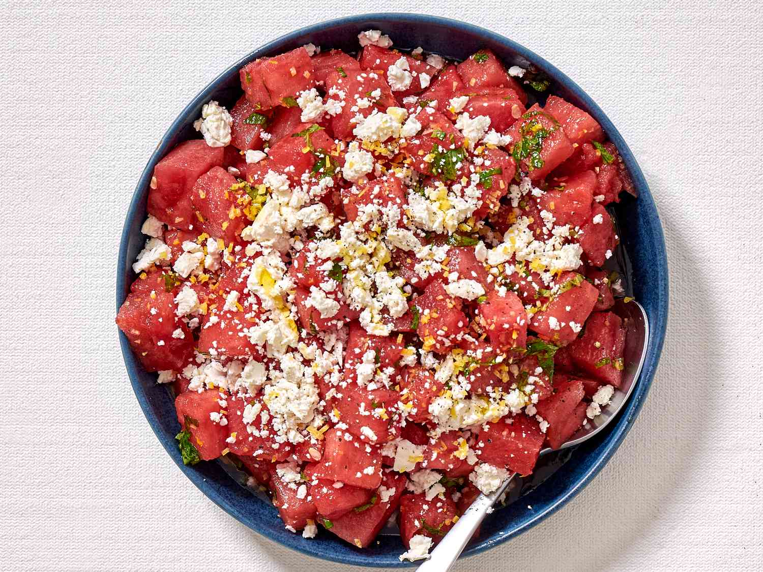 A watermelon salad with feta cheese, mint, and lemon zest in a large blue bowl.