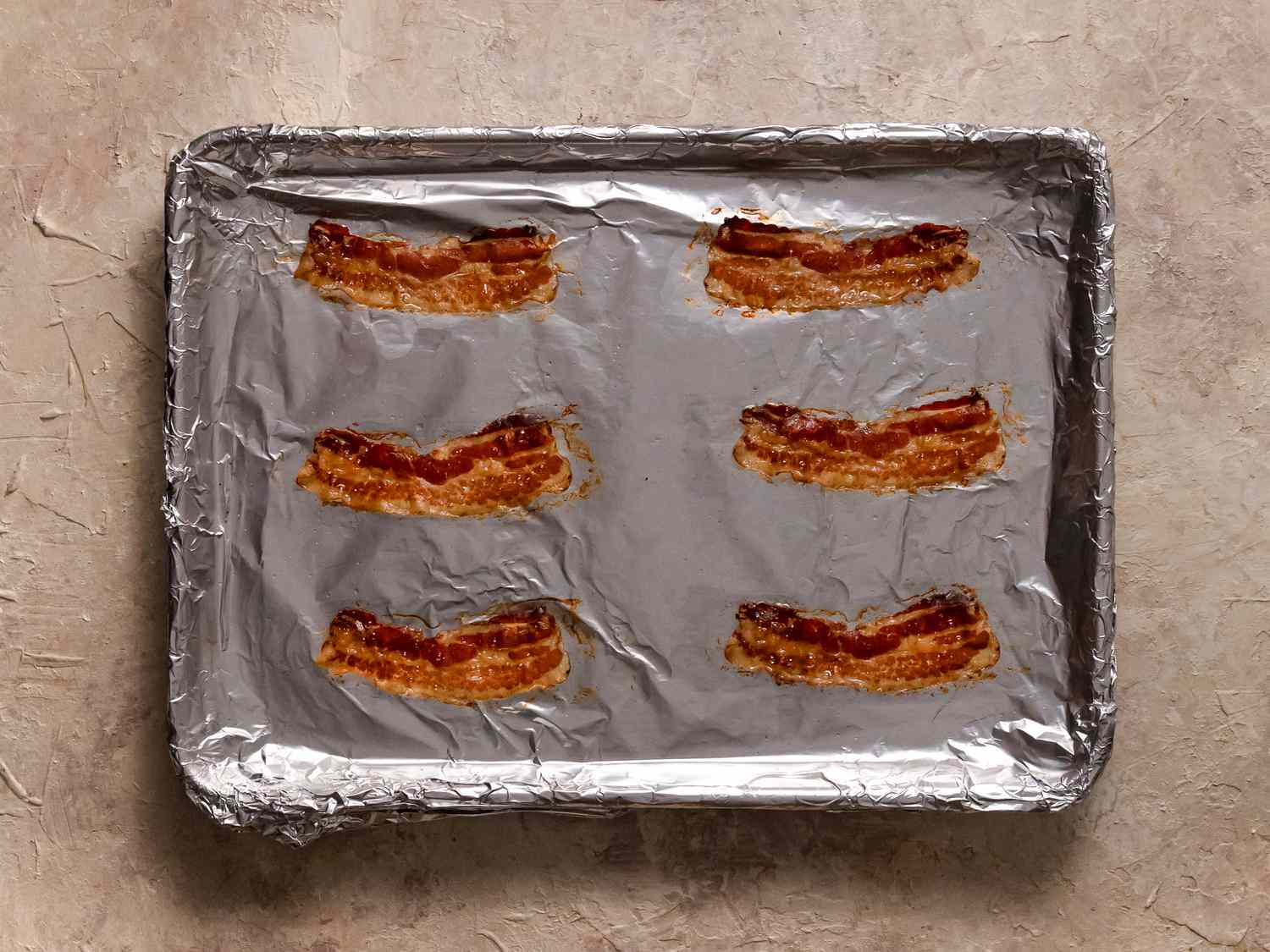 Bacon which has been cooked on a baking sheet lined with aluminum foil.