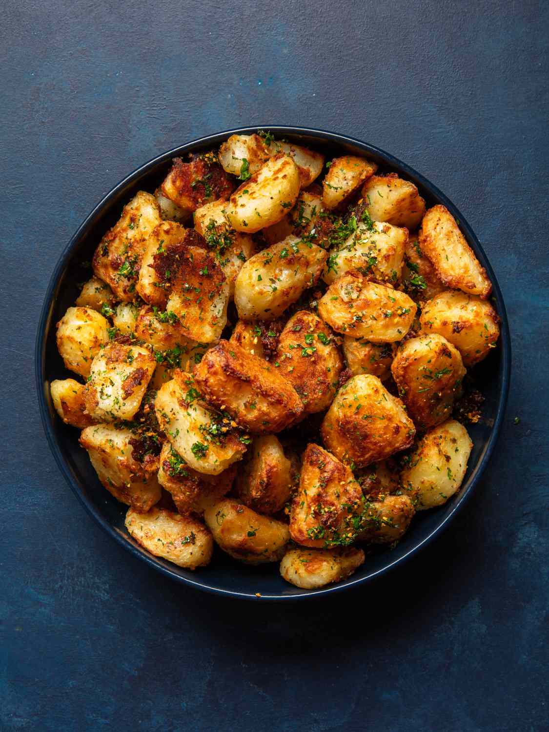 The best crispy roast potatoes ever in a blue bowl on a blue background.