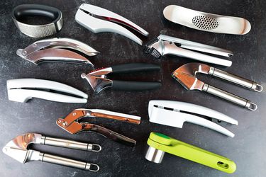 a collection of 12 different garlic presses on a counter