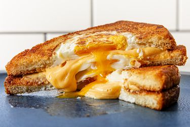 Two halves of a grilled cheese egg-in-the-hole sandwich stacked on top of each other, with cheese and egg overflowing from the middle.