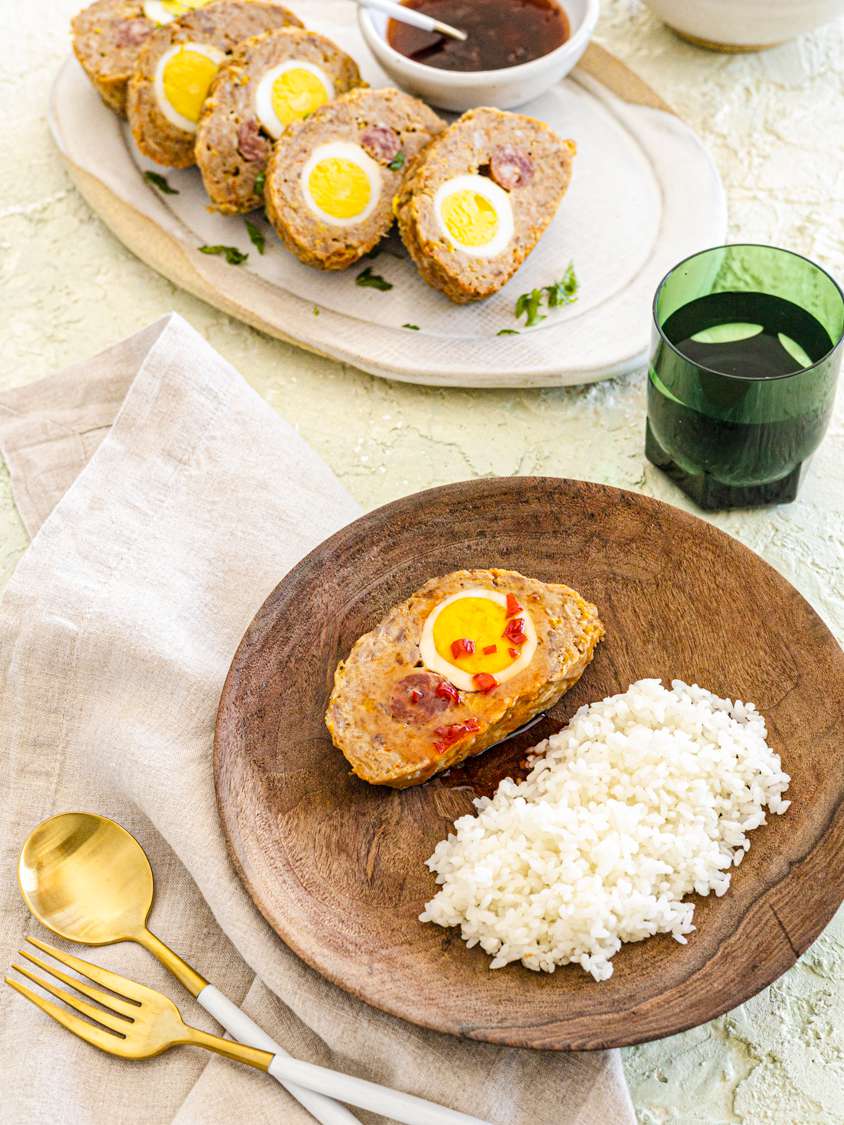 A overhead view of a tablescape with a serving plate of embutido and a plate with a single serving of one slice of embutido and rice