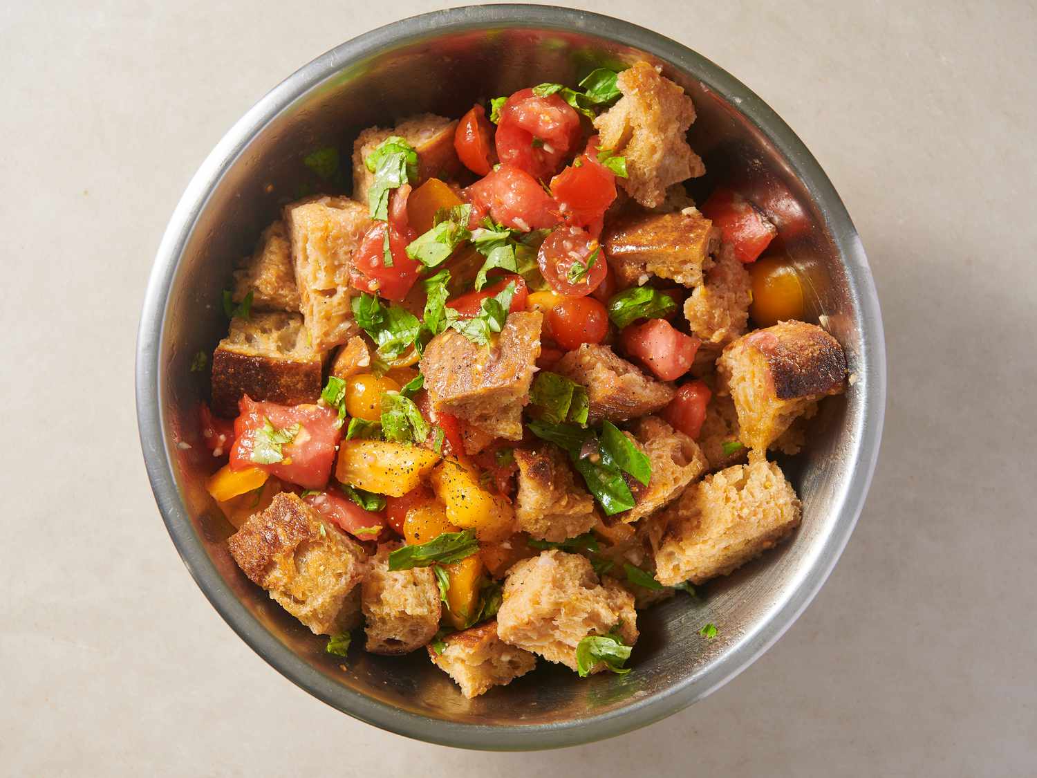 Toasted bread, tomatoes, dressing, and basil leaves tossed inside a large bowl and seasoned with salt and pepper