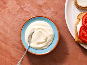 Two-minute mayonnaise in a serving bowl with a spoon, with an open face tomato sandwich on the right edge of the frame