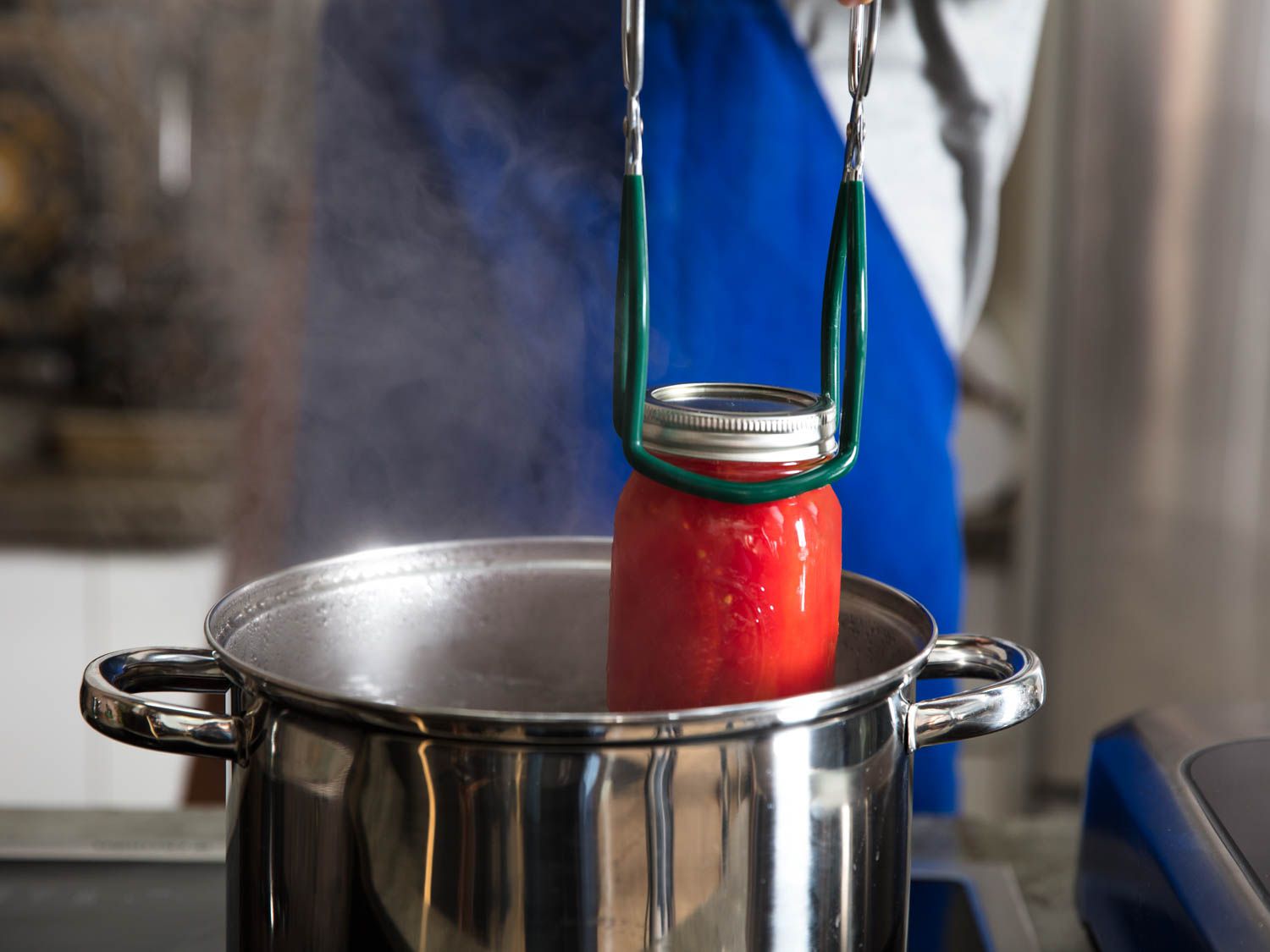 A jar of processed tomatoes being lifted out of a water bath with a pair of jar tongs.