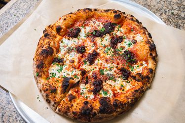 Nduja pizza cooked in outdoor pizza oven on a piece of parchment set on a pizza pan