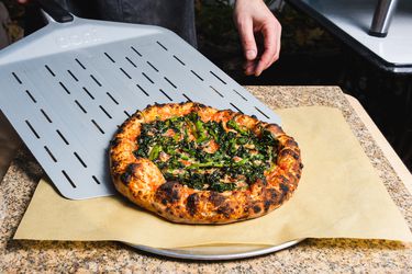 Sliding a charred broccoli rabe pizza onto a serving tray