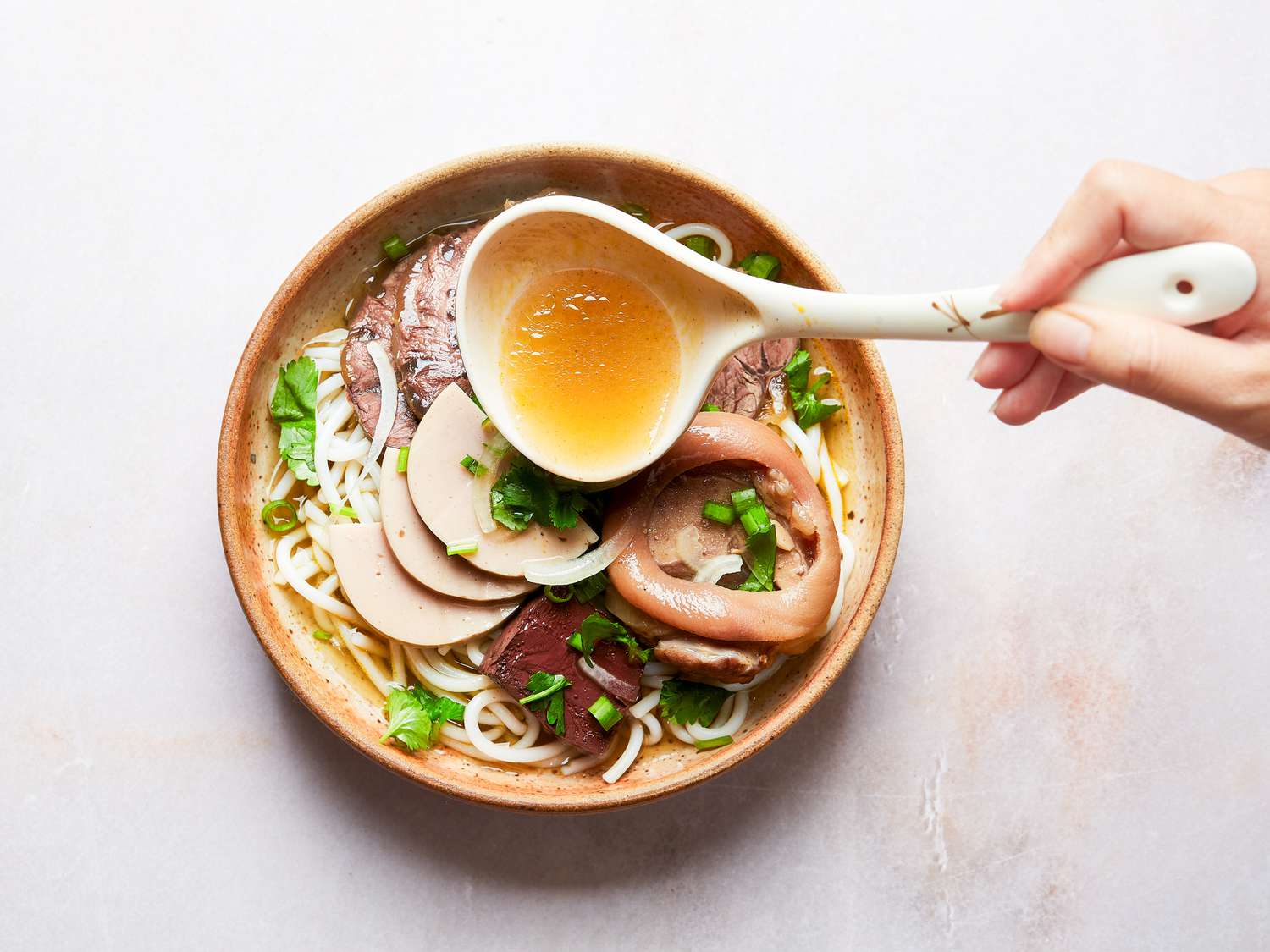 Overhead view of ladling broth into prepared Bun Bo hue bowl