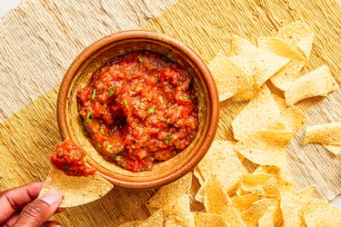 Overhead view of a hand dipping a chip in salsa