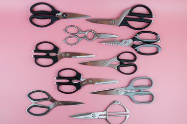 ten different kitchen shears lined up on a pink background