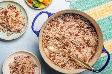 Overhead view of a pot of Jamaican rice and peas with a serving spoon, two serving plates and a green and yellow fabric