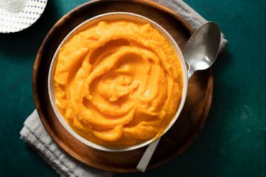 Butternut squash purÃ©e in a white bowl next to a large spoon.