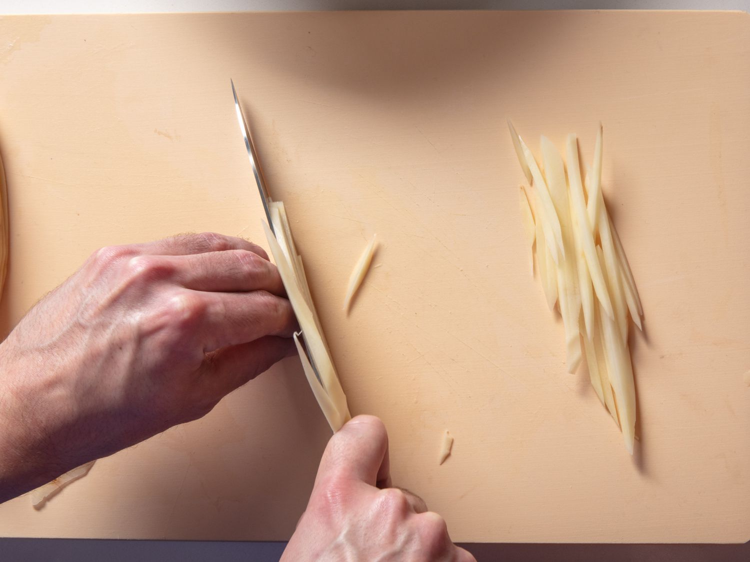 Cutting planks of potato into shoestring fries on a cutting board