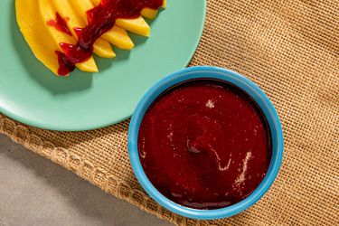 Chamoy in a bowl next to a plate of sliced fresh mango drizzled with chamoy